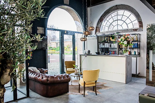 De entree met een chesterfield, twee mosterdgele stoelen en het waaiervenster